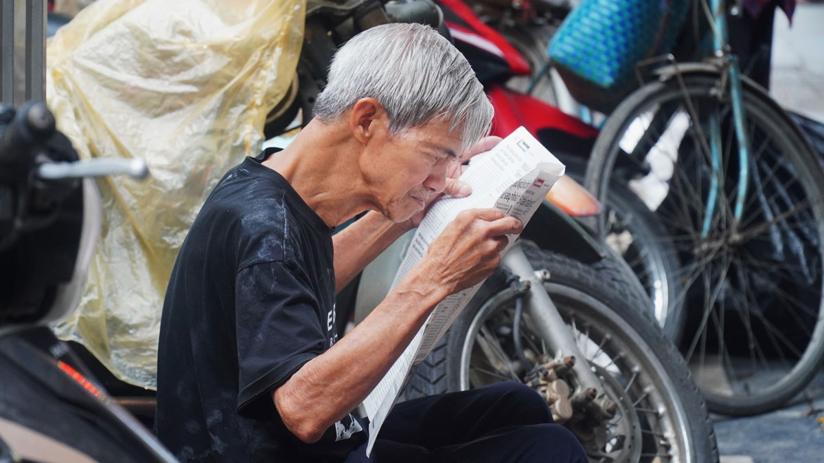 Slowly flipping through each newspaper page, the old man enjoys a peaceful time in the heart of the city. Photo: Minh Vu