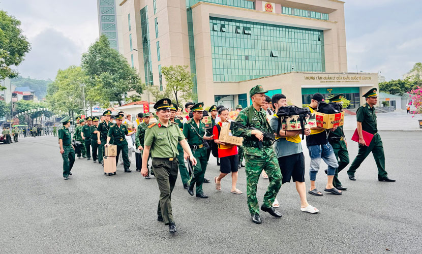 Lực lượng chức năng dẫn giải 19 đối tượng qua cửa khẩu quốc tế Lào Cai. Ảnh: Thanh Tuấn
