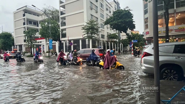 Hanoi people struggle to wade through flooded water after rain. Photo: Long Phi