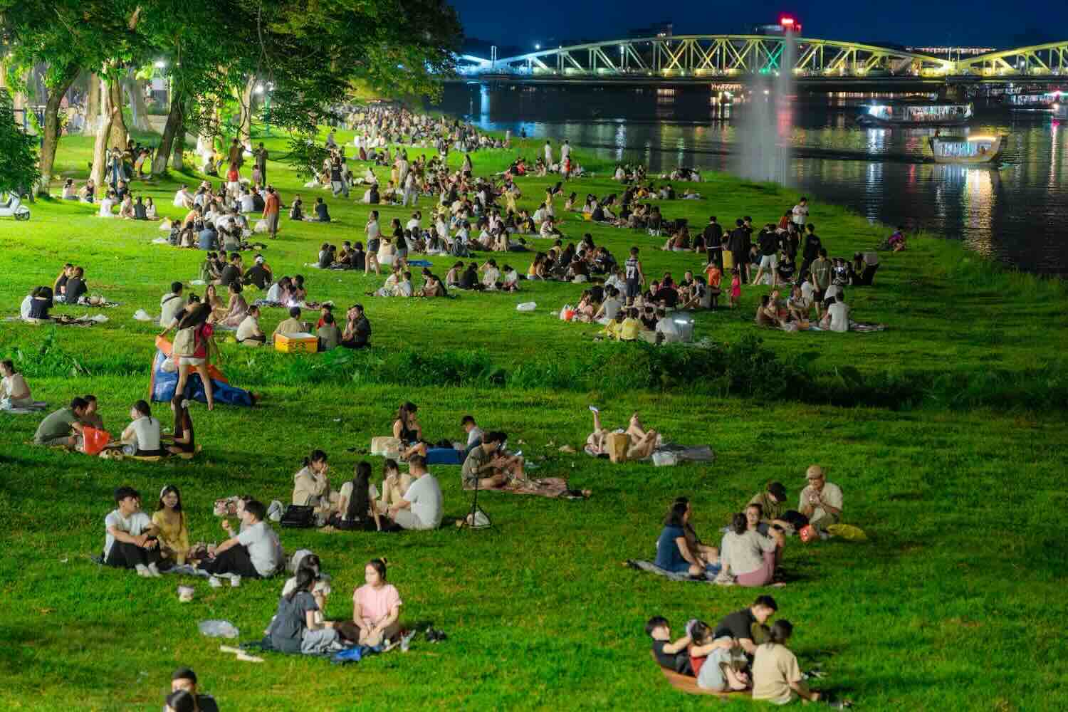 People and tourists relax on the grass along the poetic Perfume River. Photo: Hue City People's Committee.