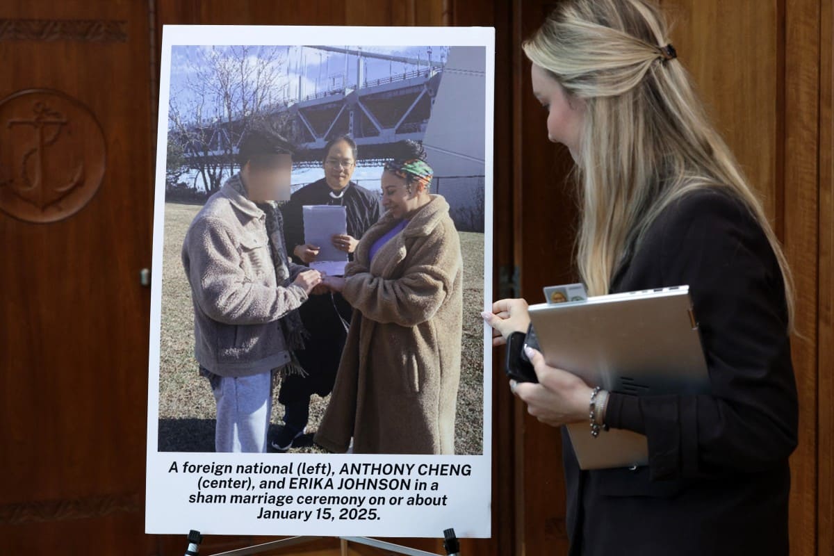 An employee of the US Department of Justice displays a poster with images of suspects in a marriage fraud ring at a press conference at the US Department of Justice on August 12, 2026, in Washington DC. Photo: AFP
