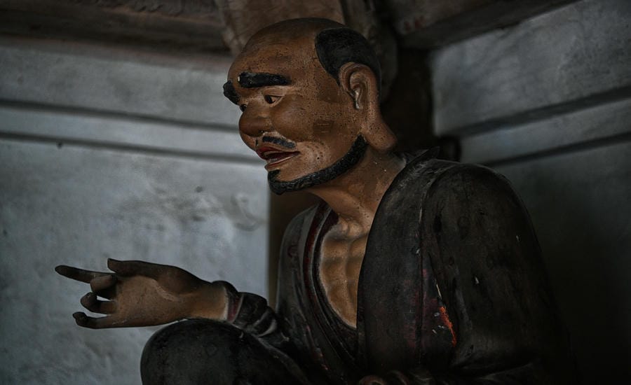 La Hán nghiêng mình, bàn tay mở ra như đang giảng giải, đối thoại với người đứng trước mặt.