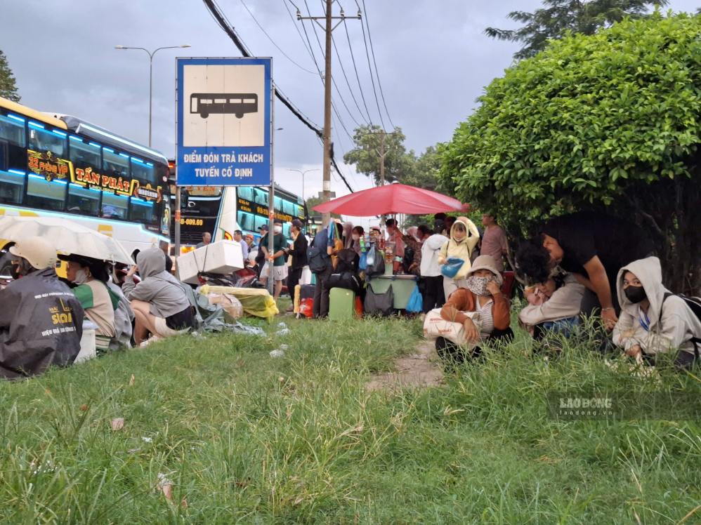 Gente refugiándose de la lluvia bajo los arbustos mientras esperan coches en la Carretera Nacional 1, frente a la Zona de Procesamiento de Exportaciones Linh Trung 1. Foto: Minh Quân