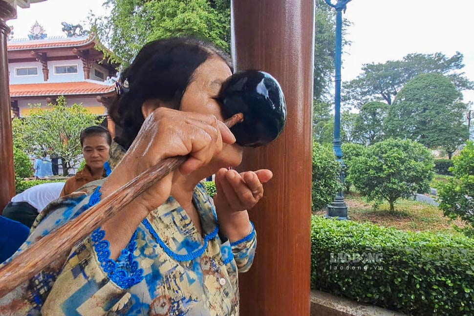 Bà Đỗ Thị Sáu uống nước giếng cổ, cầu mong bình an và sức khỏe. Ảnh: Đinh Trương