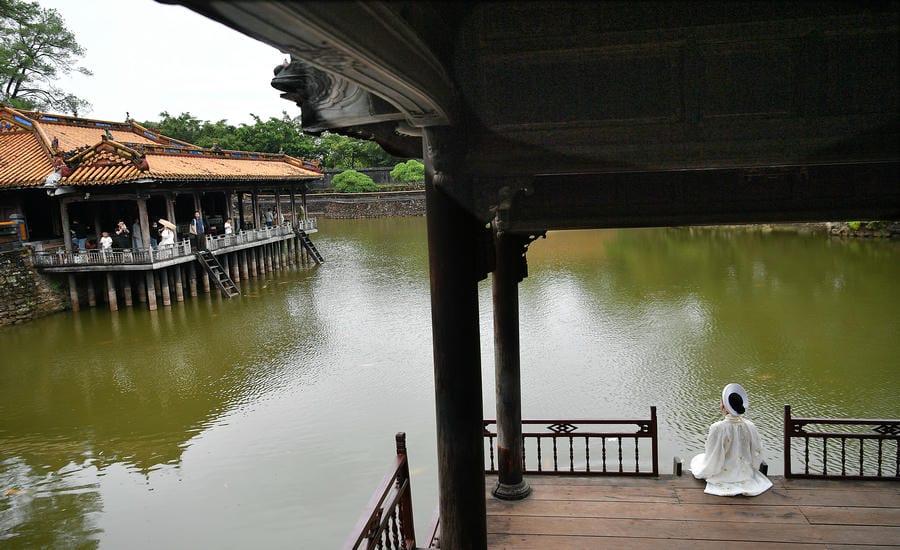 Một bạn trẻ trong trang phục áo dài ngồi bên hồ, tạo nên sự giao thoa thú vị giữa không gian cung đình xưa và đời sống hôm nay.