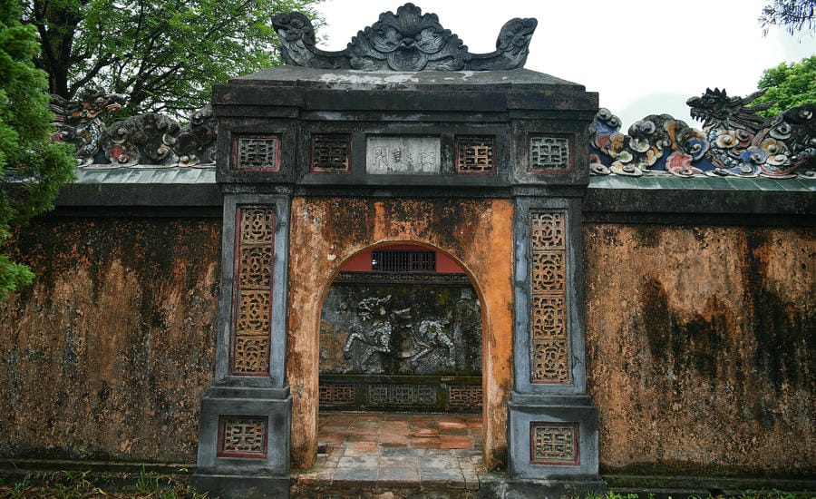 Tự Khiêm Môn với lối kiến trúc cổng vòm bằng gạch rêu phong cổ kính. Qua vòm cổng là bức bình phong đắp nổi hình Kỳ Lân, vừa mang ý nghĩa phong thủy che chắn, vừa tạo nên vẻ trầm mặc cho quần thể Lăng Tự Đức.