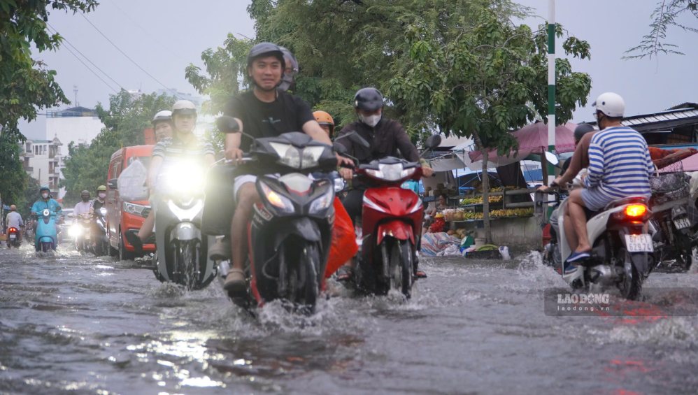 Người đi xe máy phải giảm tốc độ khi qua đoạn đường ngập sâu.