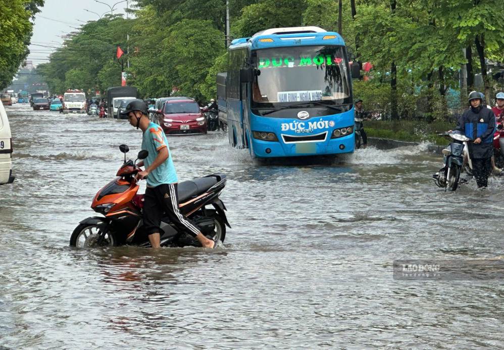 People lead motorbikes through the flooded area near the Tram Troi town (old) intersection on the morning of September 18. Photo: To The