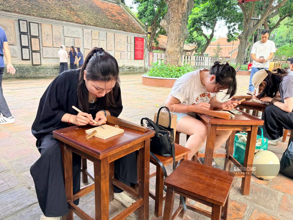 Du khách chăm chú chạm khắc những họa tiết truyền thống trên phôi gỗ tại Văn Miếu – Quốc Tử Giám. Ảnh: Thảo Anh
