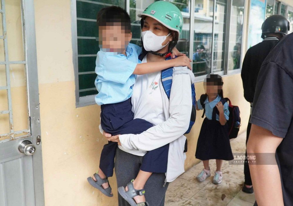 Parents carry their children into class on the morning of September 23rd because the schoolyard was flooded after heavy rain. Photo: Chan Phuc