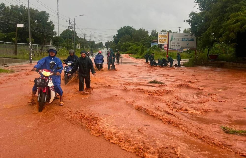 Lực lượng chức năng phường Phú Thủy hỗ trợ người dân qua khu vực dòng chảy cát đỏ tràn xuống đường chiều 23.9. Ảnh: Hữu Lệnh