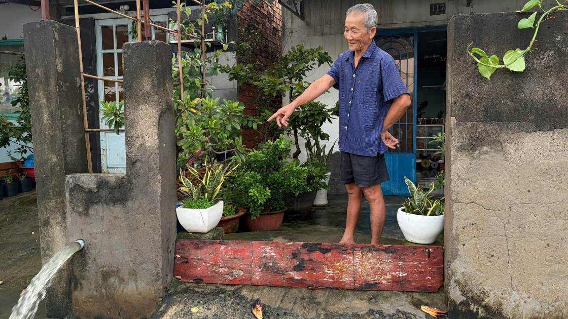Ông Dương Văn Khiêm đứng bên máy bơm, xả nước từ trong nhà ra đường. Máy bơm được gia đình ông chuẩn bị từ khuya để ứng phó với triều cường. Ảnh: Thái Bảo