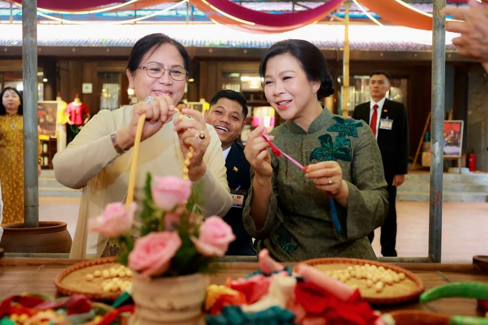 Hai phu nhân trải nghiệm xâu vòng lụa. Ảnh: Bộ Ngoại giao