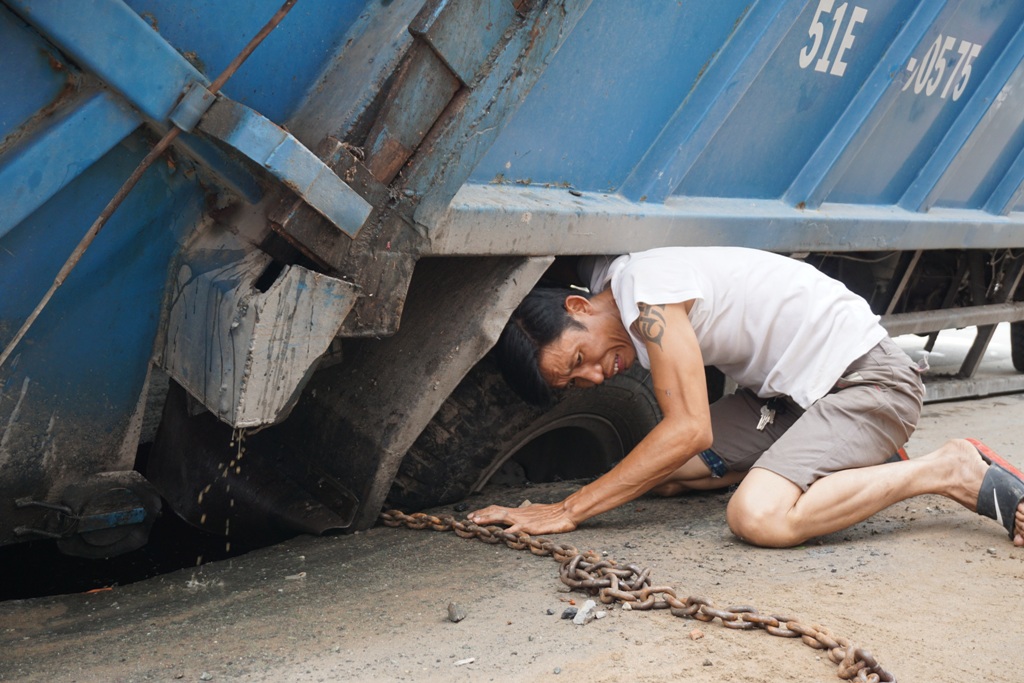 Lực lượng cứu hộ buộc dây xích vào bánh sau xe rác để nâng lên khỏi hố.  Ảnh: M.Q