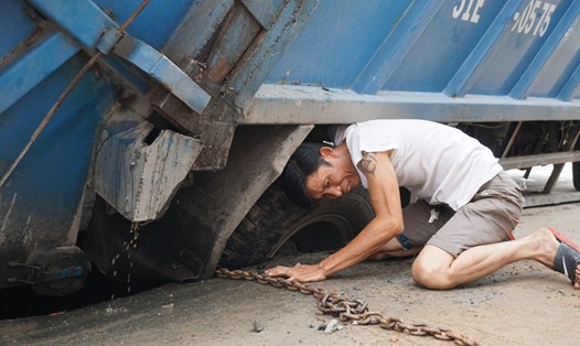 Lực lượng cứu hộ buộc dây xích vào bánh sau xe rác để nâng lên khỏi hố.  Ảnh: M.Q
